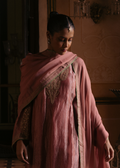 Woman in a pink traditional outfit with intricate designs, standing indoors.